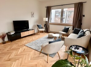 Una sala de estar moderna con un televisor de pantalla plana, dos sofás, una mesa de centro y un ventanal con cortinas.