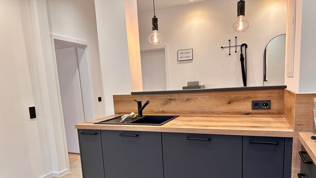 A modern kitchen with a wooden countertop, black cabinets, and pendant lighting. - Apartment 'The Pureness 1' with Shared Garden, Balcony and Wi-Fi (Hildesheim)