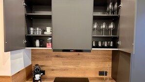 A kitchenette with a coffee machine, a Siemens induction cooktop, and a cabinet with shelves containing glasses and plates. - Apartment 'The Pureness 1' with Shared Garden, Balcony and Wi-Fi (Hildesheim)