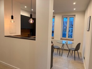 Une cuisine moderne avec des luminaires suspendus, un coin repas doté d’une table en verre et une vue par la fenêtre.