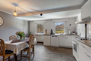 Una cucina con mobili bianchi, un tavolo da pranzo con sedie, un lampadario e una finestra con vista sull'esterno.
