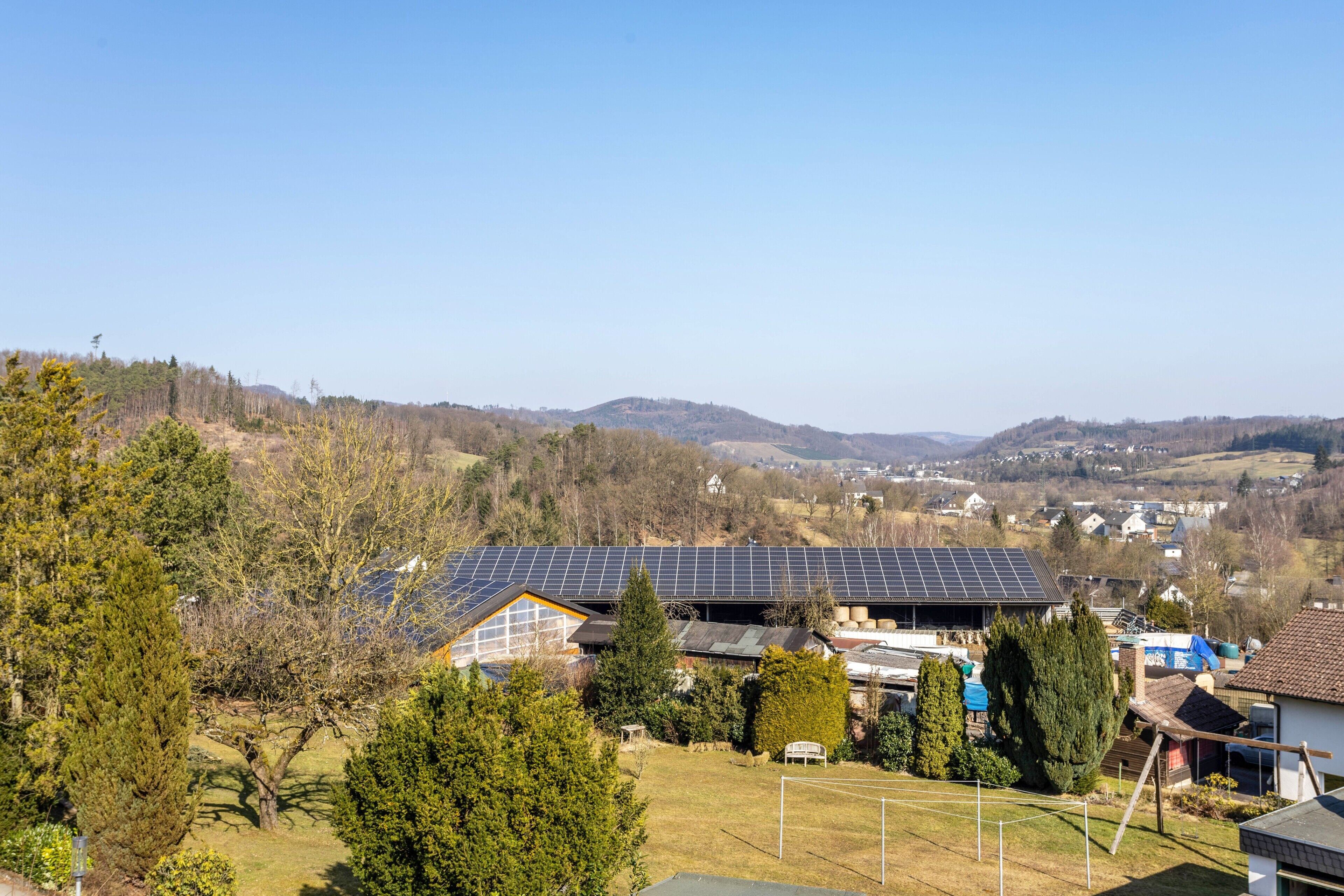 Zona residencial con paneles solares en el techo de una casa, rodeada de árboles y colinas.