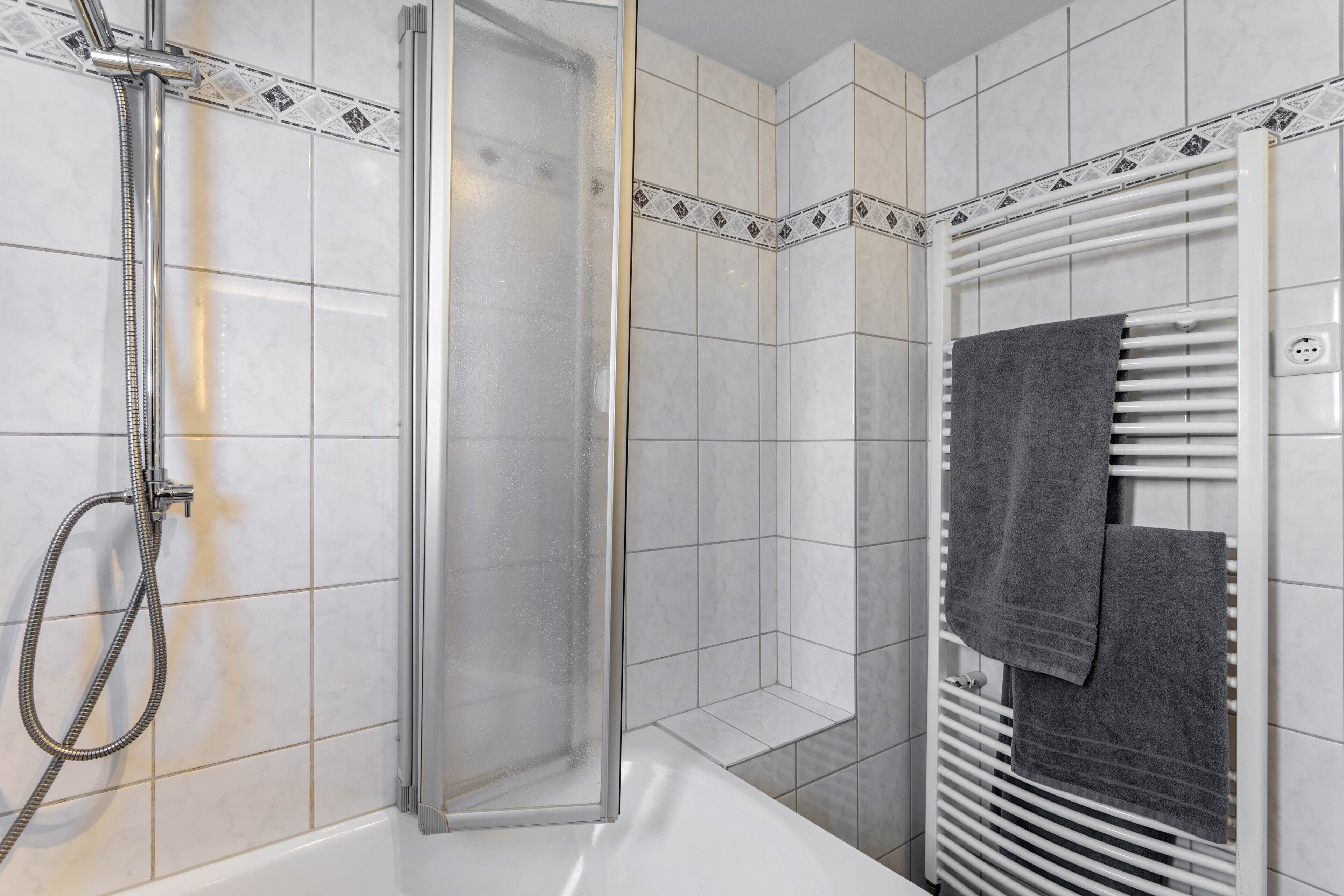 Een douche met een glazen deur, een handdoekrek met handdoeken en een witte betegelde wand.
