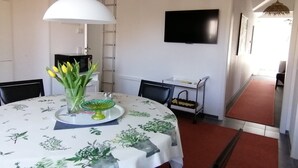 A dining area with a round table, chairs, a white tablecloth, a vase with flowers, a hanging light, a TV on the wall, and a red carpet. - Apartment '2' with Shared Garden and Wi-Fi (Meersburg)
