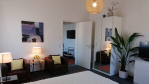 A modern living room with a sofa, armchairs, a coffee table, a TV, a large potted plant, and a hanging light fixture. - Apartment '2' with Shared Garden and Wi-Fi (Meersburg)