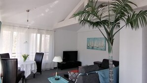 A living room with a TV, sofa, dining table, chairs, a lamp, and a large plant. - Apartment '2' with Shared Garden and Wi-Fi (Meersburg)