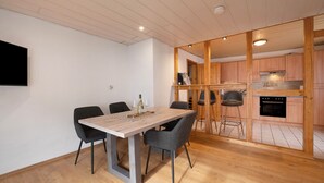 A dining area with a wooden table and chairs, a kitchen visible through an open partition, and a mounted flat-screen TV on the wall. - Apartment 'Kaamter Ferkelsmarkt' with Wi-Fi (Zell an der Mosel)