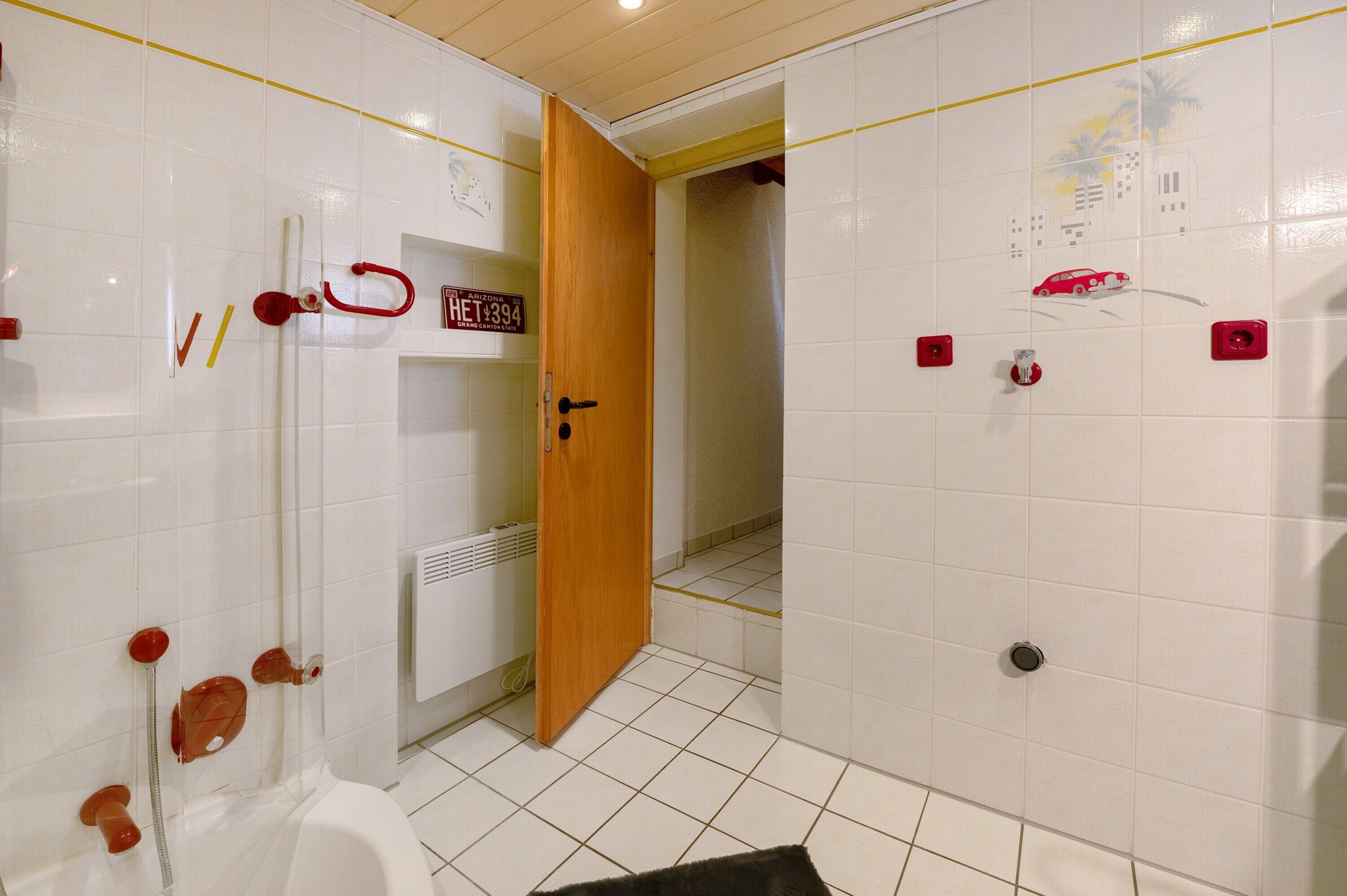 Een badkamer met witte betegelde wanden, een houten deur, een toilet en een douchehoek.