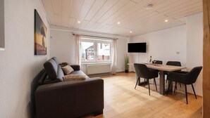 A modern living room with a sofa, dining table, chairs, a flat-screen TV, and a large window. - Apartment 'Kaamter Ferkelsmarkt' with Wi-Fi (Zell an der Mosel)