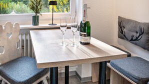 A wooden table with two glasses and a bottle of champagne, a potted plant, and a window with a view of greenery. - Vacation apartment "O" Black Forest - relaxation in a fantastic location (Münstertal/Schwarzwald)