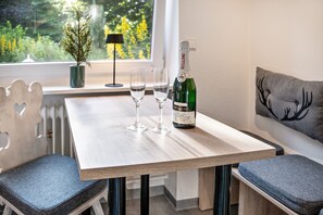 A wooden table with two glasses and a bottle of champagne, a potted plant, and a window with a view of greenery.