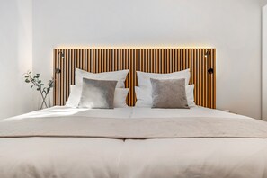 A bed with a wooden headboard, white bedding, and two bedside lamps.
