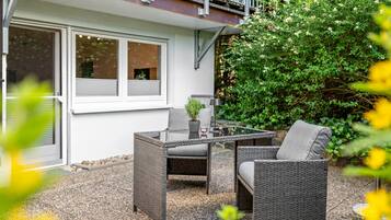 Eine Terrasse im Freien mit Korbmöbeln, einem Tisch und einem Blumentopf.