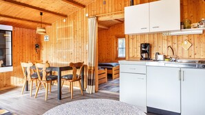 Een houten interieur met een eettafel, stoelen, een bank, een keukenhoek en een raam.