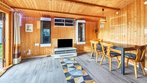 Een kamer met houten lambrisering, een flatscreen televisie, een eettafel met stoelen en een geometrisch vloerkleed.