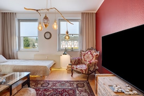 Une chambre à coucher avec un lit, une chaise, une télévision, une fenêtre et une lampe.