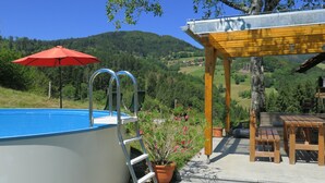 Une piscine agrémentée d’un parasol rouge, d’une pergola en bois et offrant une vue sur un paysage vallonné.