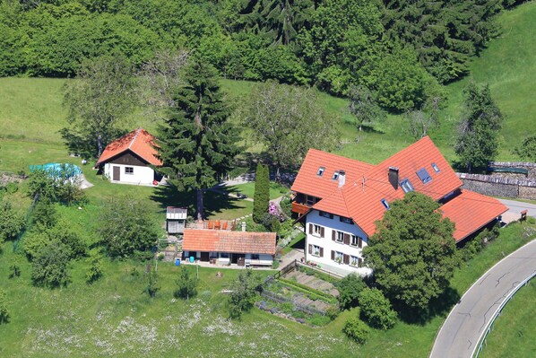 Área residencial com duas casas, uma com telhado vermelho e outra com fachada branca, cercada por vegetação e uma estrada sinuosa.