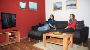 Un salon avec un mur rouge, un canapé noir, une table basse en bois et un téléviseur posé sur un meuble.