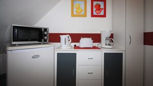 Une petite cuisine équipée d’un four à micro-ondes, d’une machine à café et d’une bouilloire, le tout posé sur un plan de travail blanc. On trouve deux placards sous le plan de travail.