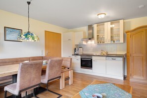 Une cuisine moderne avec des meubles blancs, un four encastré et un coin repas comprenant une banquette et des chaises.
