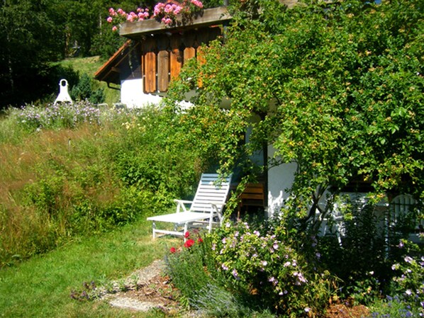 Un chalet rustique doté d’un balcon en bois, d’une chaise blanche et d’une végétation luxuriante.