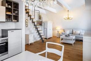 Une cuisine moderne dotée d’un four encastré, un coin repas avec une table et des chaises blanches, un escalier au design original et un salon avec un canapé et une lampe.