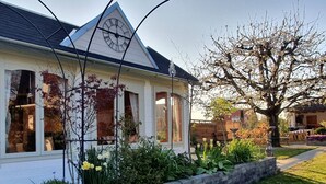 Ein Haus mit einer Uhr an der Vorderseite, ein Garten mit verschiedenen Pflanzen und ein Baum in voller Blüte.