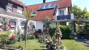 Ett hus med ett rött tegeltak, solpaneler, en trädgård med rosor och en pergola.