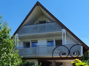 A two-story building with a balcony, a triangular roof, and a decorative metal railing.