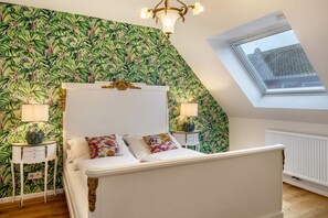 A bedroom with a bed, a skylight, a radiator, and a wall with a tropical wallpaper pattern.