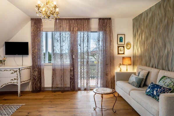 A living room with a sofa, a TV, a chandelier, a round table, and curtains.