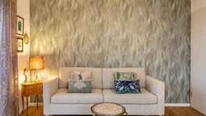 A living room with a sofa, a side table with a lamp, and a patterned wall. - Holiday Apartment 'Lavender' with Shared Garden, Balcony and Wi-Fi (Vogtsburg im Kaiserstuhl)