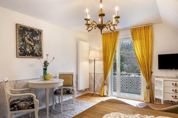 Une pièce avec un lustre, une table entourée de chaises, un téléviseur et une fenêtre avec des rideaux.