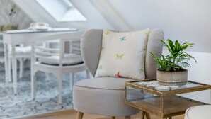 Een moderne woonkamer met een ronde grijze bank, een klein tafeltje met een plant en een wit eetgedeelte op de achtergrond.