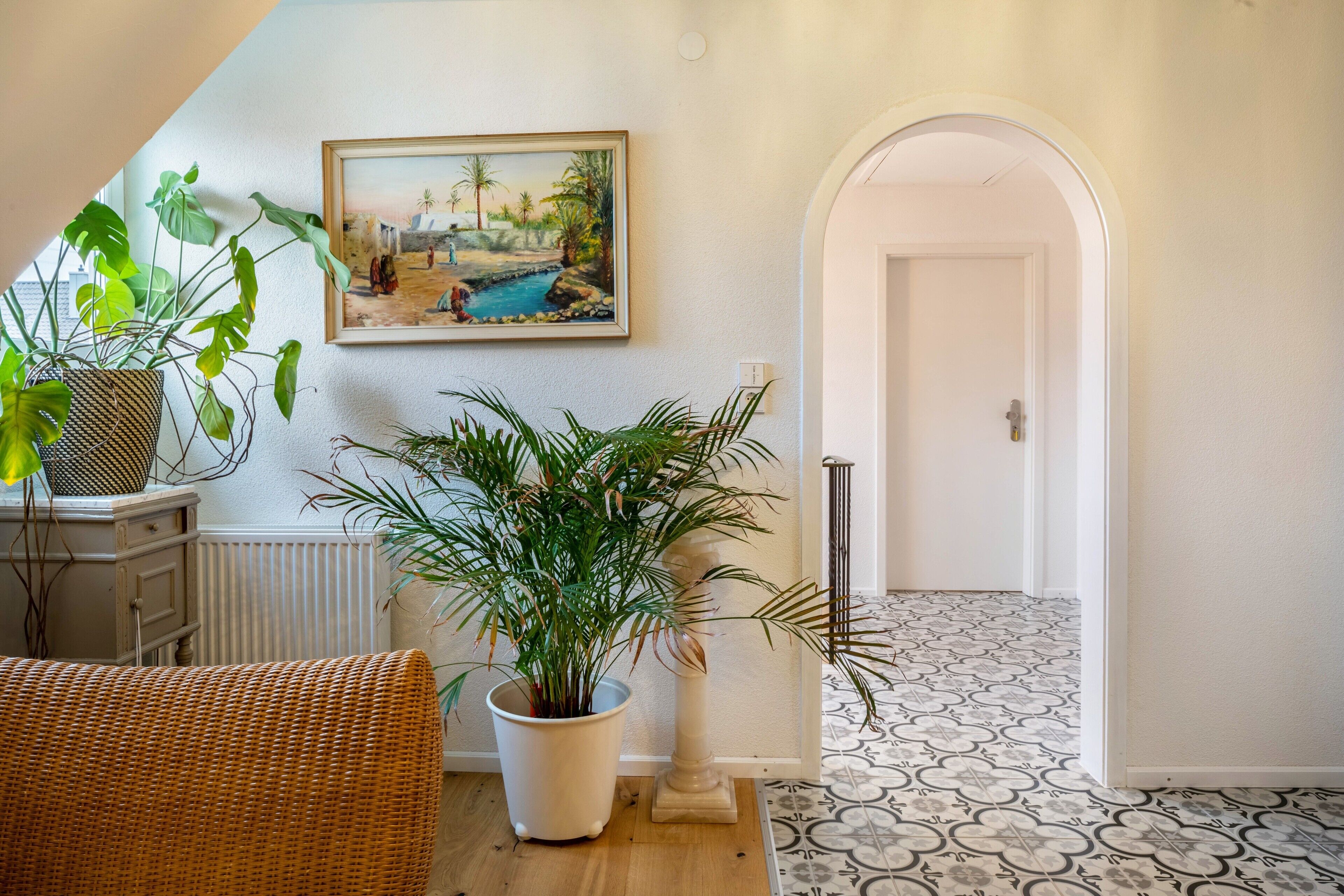 A hallway with a white door, a painting of a beach scene, and potted plants.