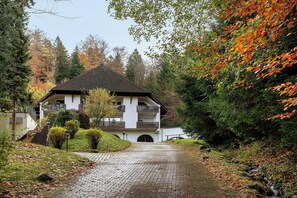 A building with a balcony, a paved pathway, and surrounding trees.