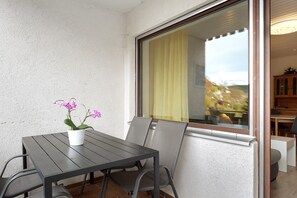 A balcony with a table and chairs, a potted plant, and a view through a window.