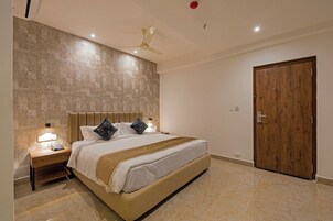 Una habitación de hotel con una cama, mesitas de noche, una puerta de madera y un ventilador de techo.