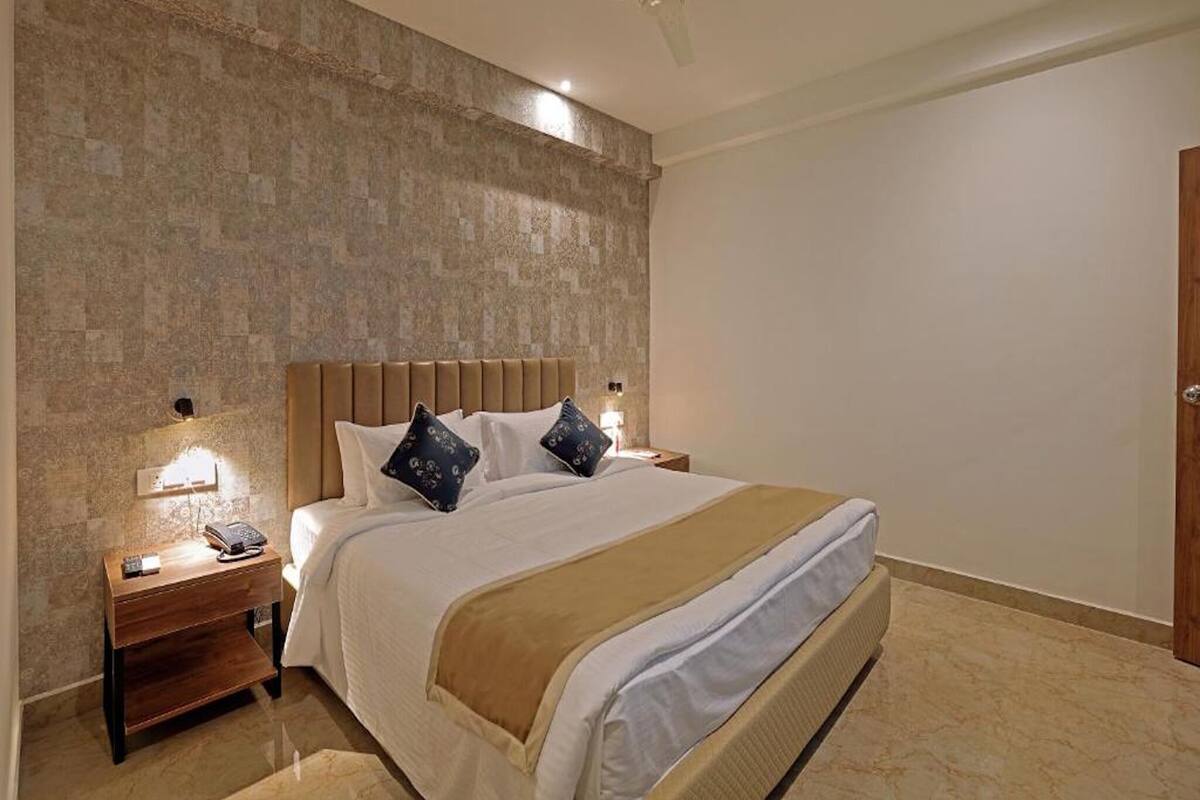A hotel room with a large bed, a wooden nightstand with a phone, a wall-mounted light, and a ceiling fan.