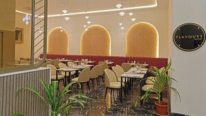 A restaurant with a modern interior, featuring a marble floor, cushioned seating, and a sign that reads "FLAVOURS DINE-IN". - Grand Continent Hotel Gachibowli, US Consulate (Hyderabad)