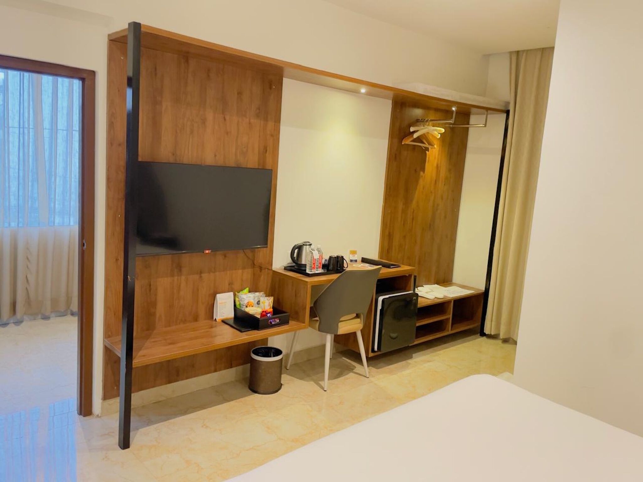 A hotel room with a wooden desk, a TV, a bed, and a wardrobe.