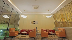 A modern lobby with a marble floor, red sofas, and a glass wall with a plant display. - Grand Continent Hotel Gachibowli, US Consulate (Hyderabad)