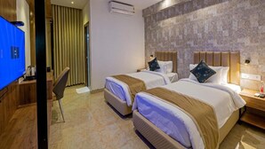 A hotel room with two beds, a TV, a desk, a chair, an air conditioning unit, and a ceiling fan. - Grand Continent Hotel Gachibowli, US Consulate (Hyderabad)