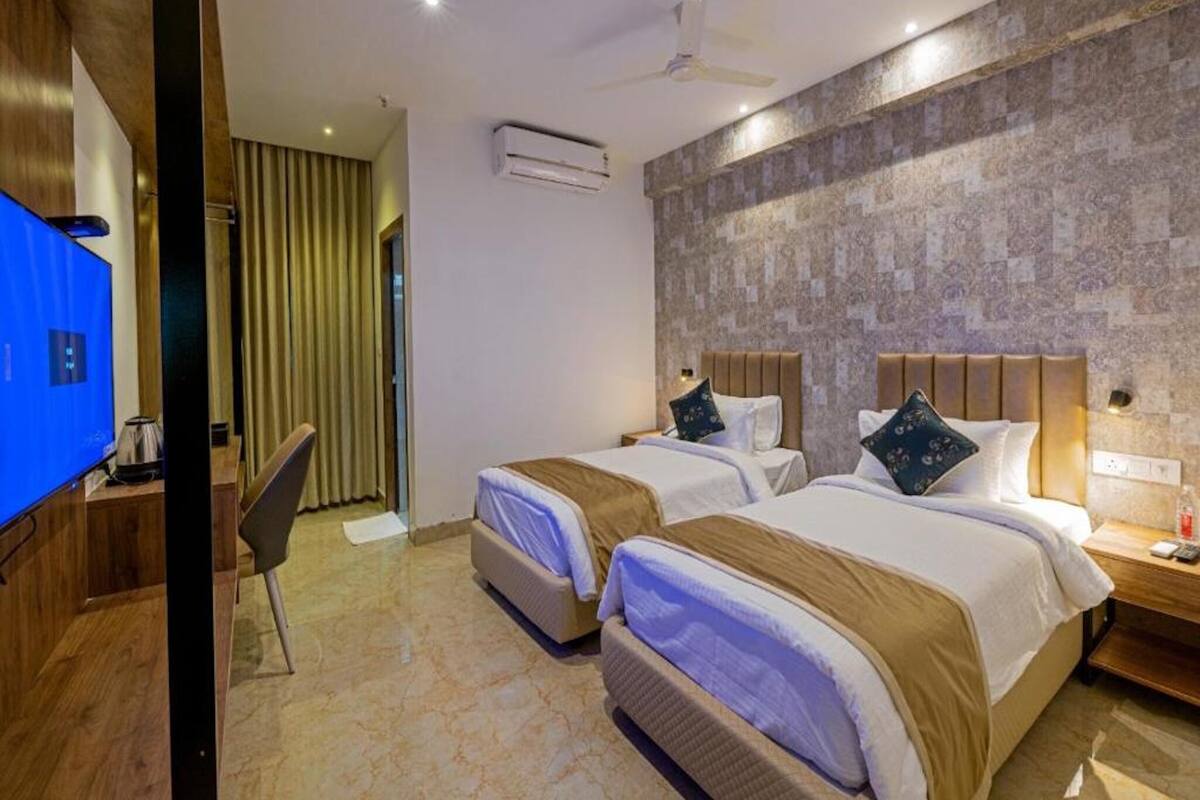 A hotel room with two beds, a TV, a desk, a chair, an air conditioning unit, and a ceiling fan.
