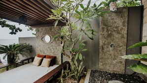 A bedroom with a wooden bed, pillows, a small plant, and a view of the sea.