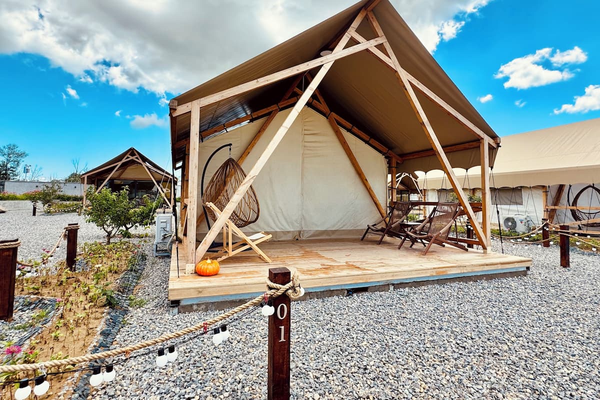 A tented accommodation with a wooden deck, a hanging chair, and a small pumpkin decoration.