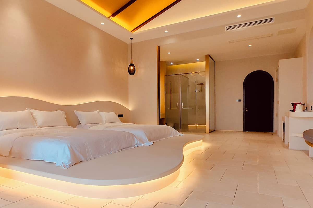 A modern bedroom with a curved bed, a glass shower enclosure, and a visible bathroom area.