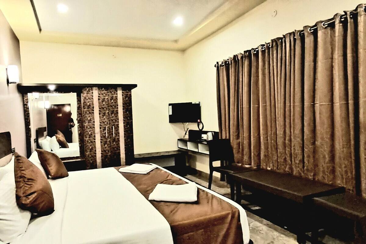A hotel room with a bed, a desk, a chair, a mirror, and a curtain.
