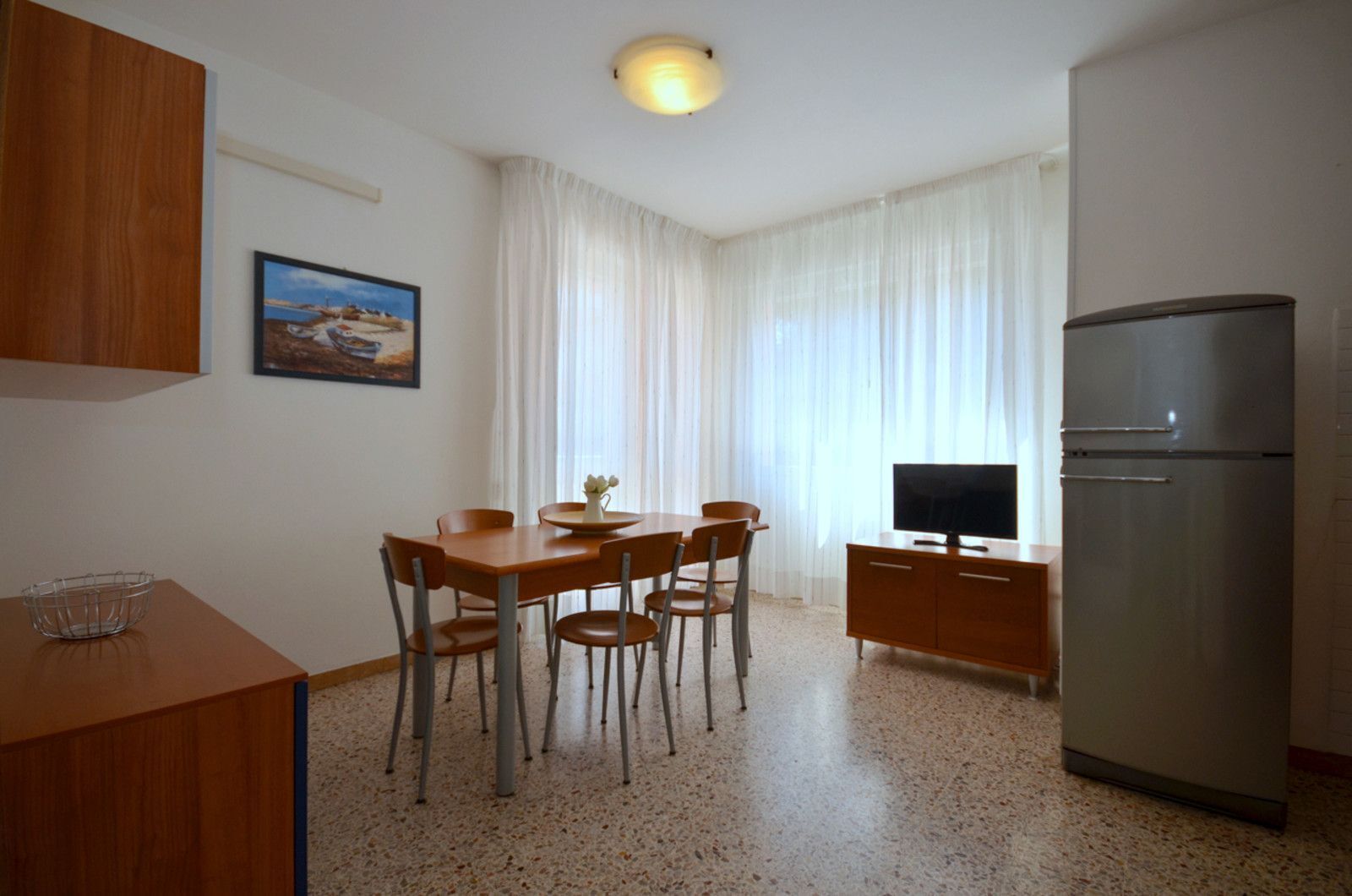 Een kleine keuken met een eettafel, stoelen, een koelkast en een televisie.